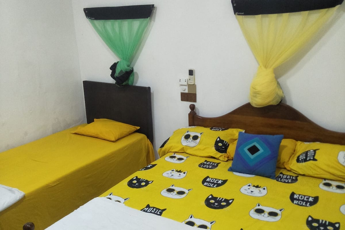 A room with two single beds, one with yellow bedding and the other with white bedding. There is a bed with a yellow and white cat-themed bedspread.