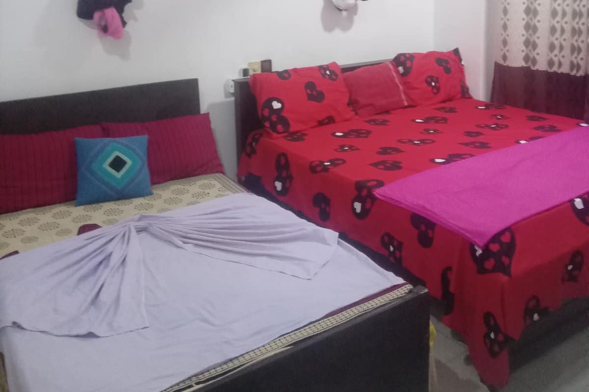 A bedroom with two beds, one with a red patterned bedspread and the other with a white bedspread. There are pillows and a blanket on the beds, and a ceiling fan is visible.