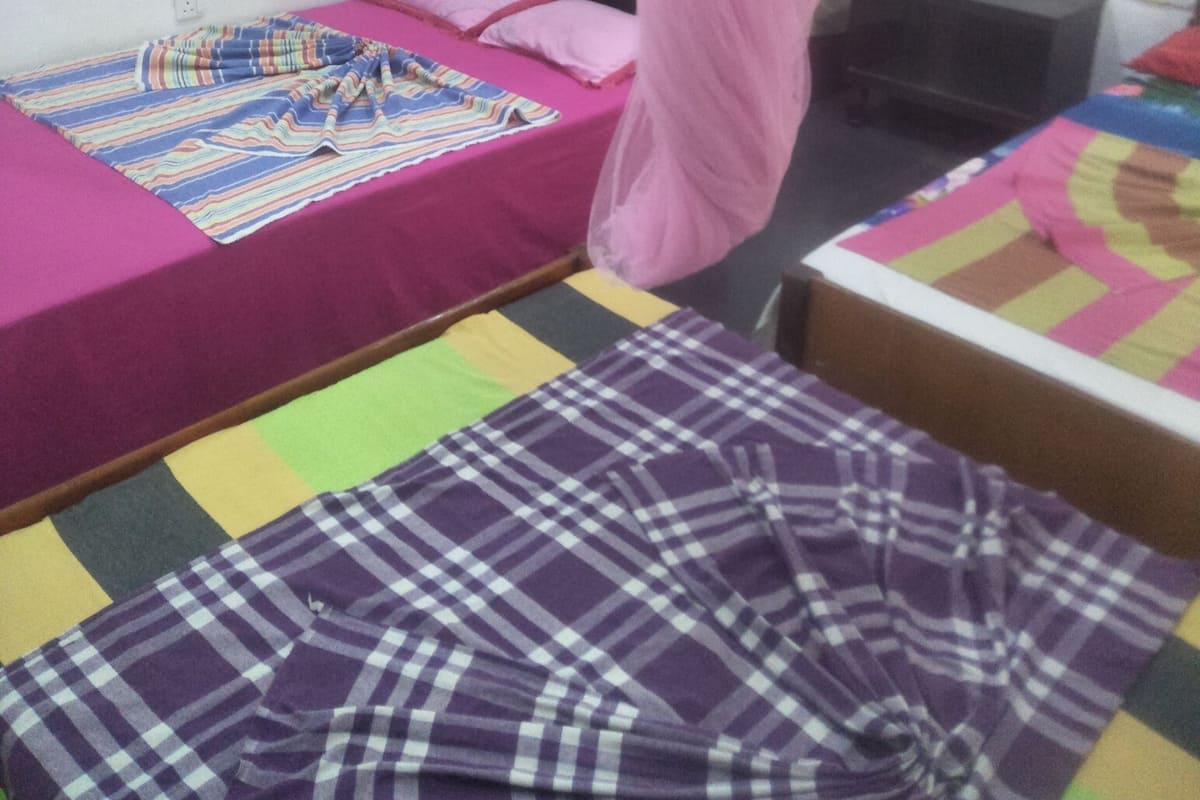 A bedroom with two beds, one with a pink canopy and another with a colorful striped bedspread.
