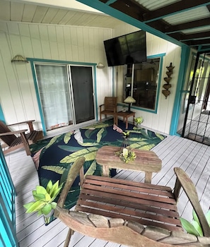 Relax in this cozy outdoor seating area with a wooden deck and patterned floor, featuring two comfortable chairs and a small table with a lamp, and a TV mounted above.
