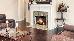 Una sala de estar con chimenea, dos sofás, una mesa de centro de cristal y un cuadro sobre la repisa.