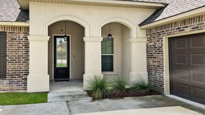 Una casa residencial con fachada de ladrillo, un porche con dos columnas y una puerta de garaje.