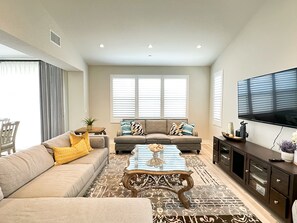 Ein geräumiges Wohnzimmer mit einem beigen Sofa, einem Glastisch und einer dunklen Holzkommode.