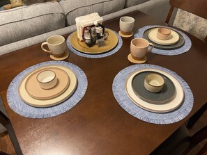 Uma mesa de jantar posta com pratos, tigelas e xícaras, com um pequeno objeto decorativo no centro.