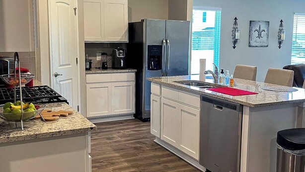 A modern kitchen with white cabinetry, a stainless steel refrigerator, a built-in dishwasher, and a granite countertop. - Spacious Home Base with Private Office—Perfect for Remote Work (Lake Charles)