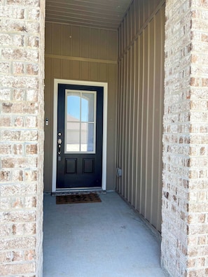 A dark-colored door with a window, flanked by brick walls and a metal siding exterior.