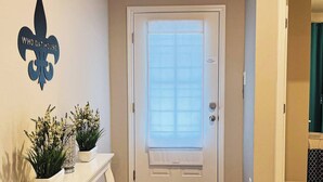 A hallway with a white door, a white console table with plants, and a wooden floor. - Spacious Home Base with Private Office—Perfect for Remote Work (Lake Charles)