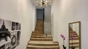 Eine Treppe mit Marmorstufen führt zu einer Zwischenebene, eine Chandelüster und ein Spiegel, der die Treppe reflektiert.