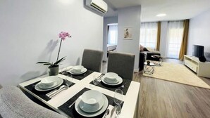 A modern dining area with a table set for four, a potted orchid, and a living area with a sofa and TV. - Casa SoHo y Alex, Apartment 2A,- 2 bedroom (Estepona)