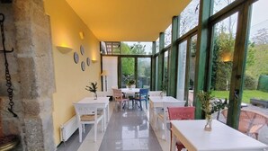 A dining area with white tables and chairs, large windows, and a stone wall. - La Villa de Palacios (Voto)