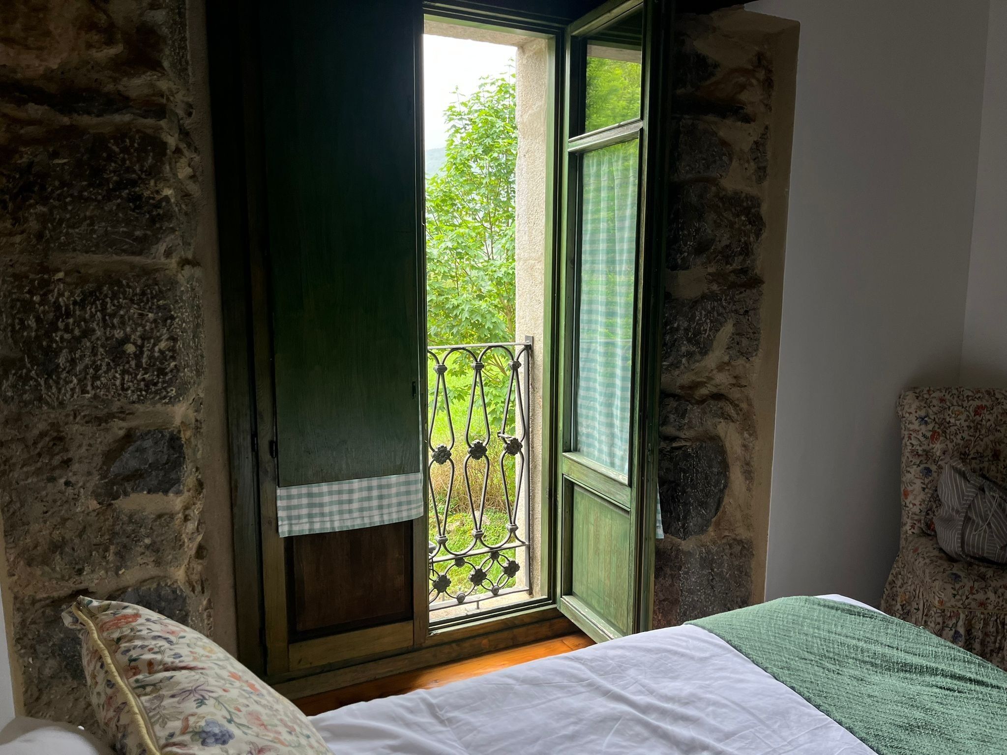 A room with a bed, a window with a checkered curtain, and a view of greenery outside.