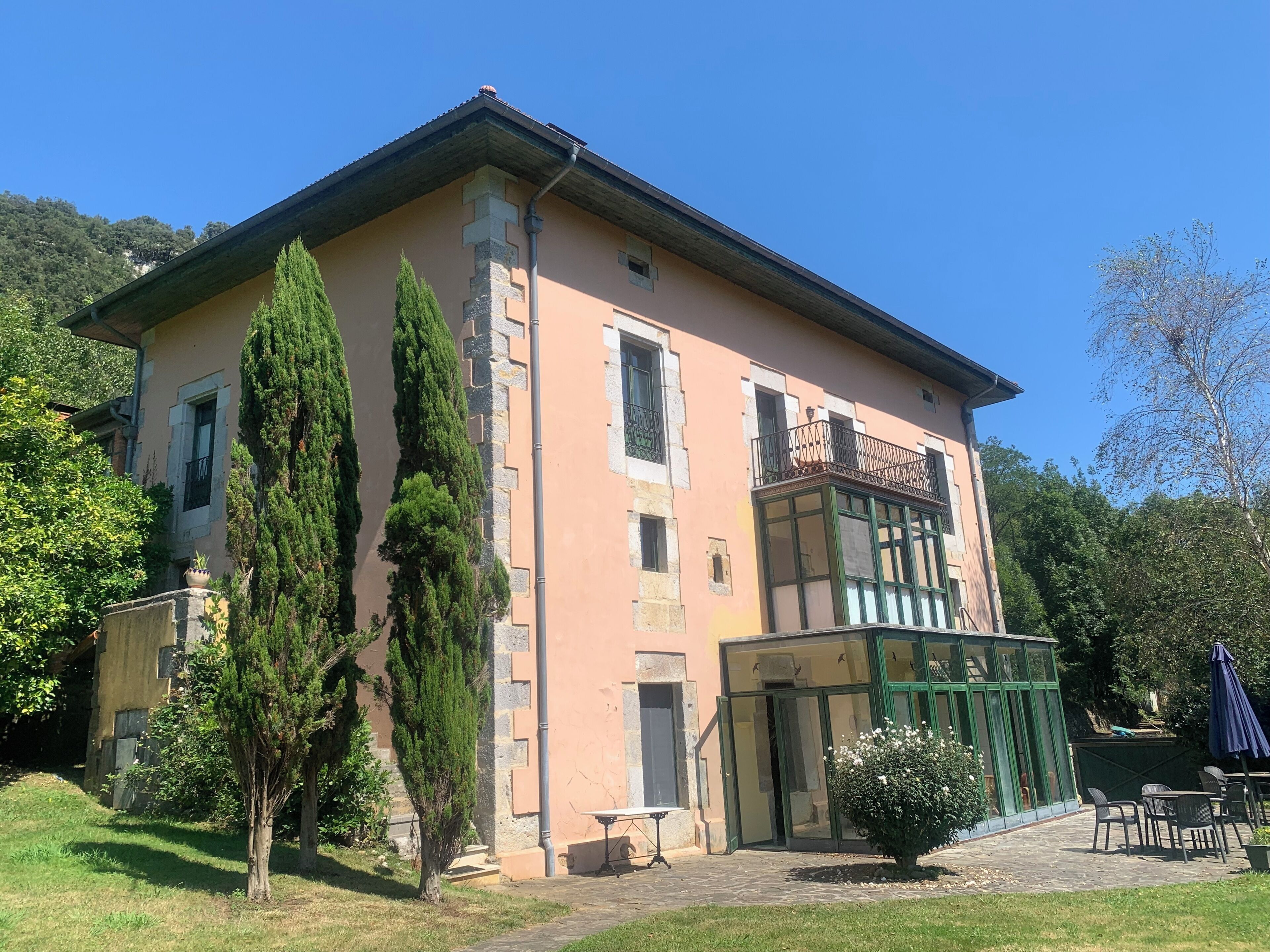 Un bâtiment à deux étages doté d’un balcon, d’une porte verte et d’un petit espace extérieur aménagé pour s’asseoir.