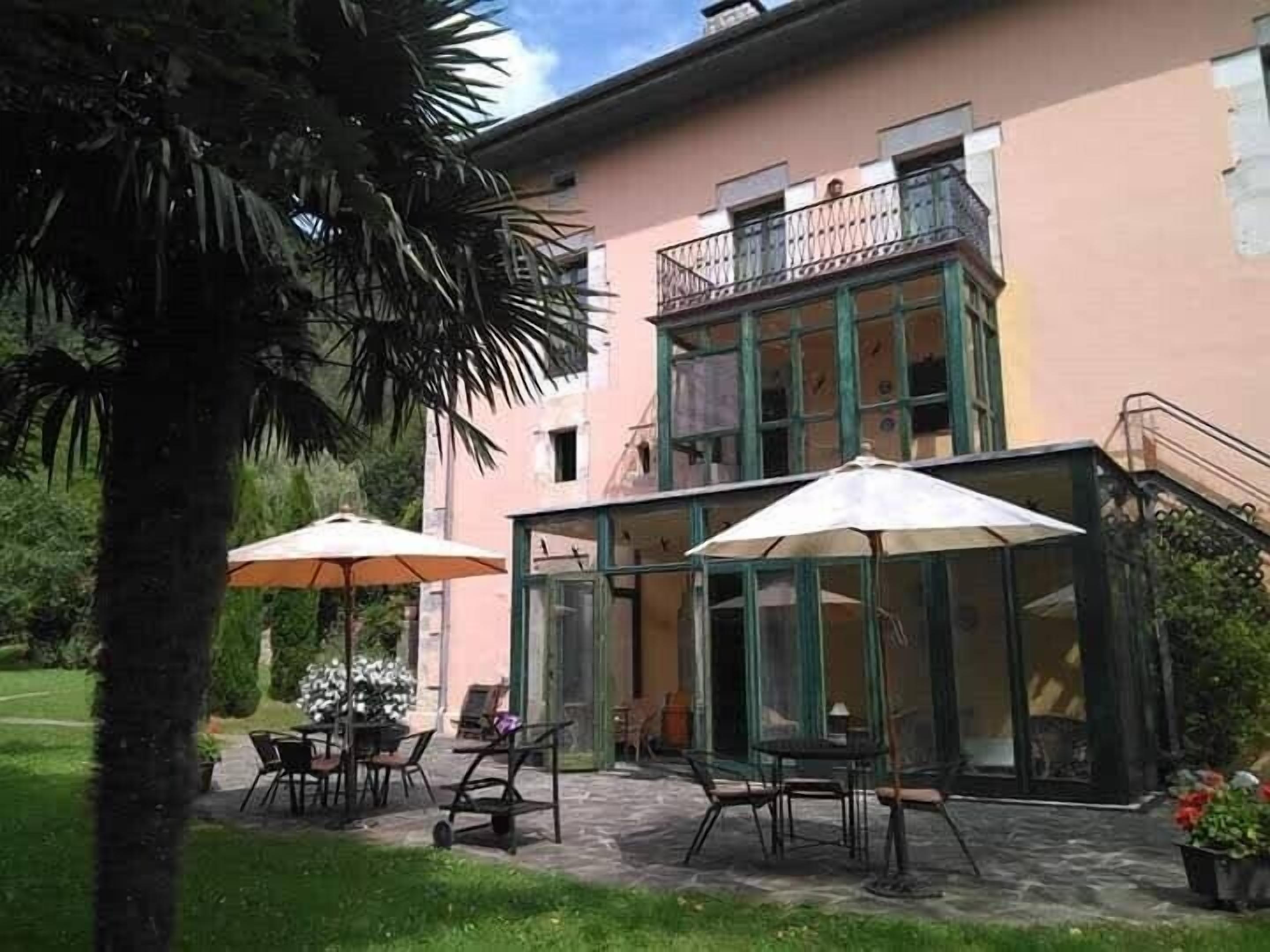 A building with a glass conservatory, outdoor seating, and a staircase leading to an upper balcony.