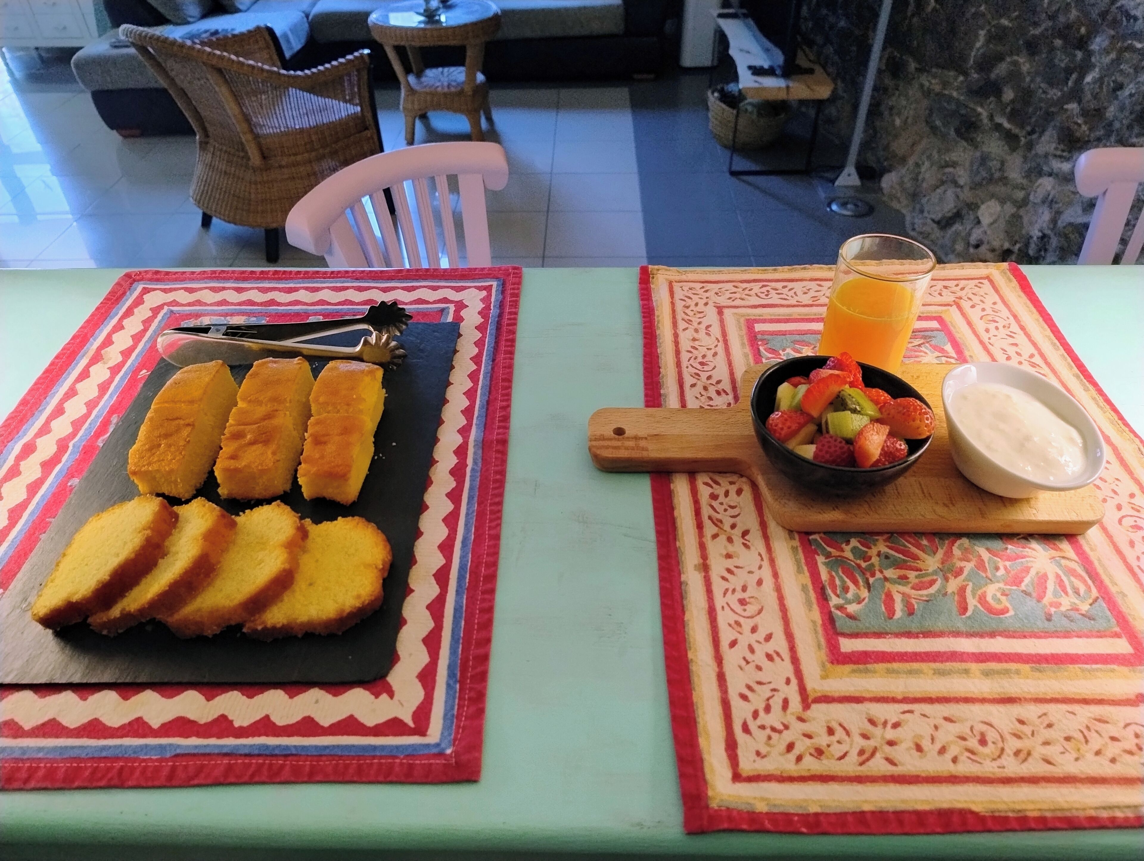 A table with a fruit bowl, a glass of orange juice, and a plate of bread.