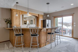 A kitchen with a central island, bar stools, wooden cabinets, and a large window. - Spacious Pool House with tons of amenities!
 (Omaha)
