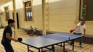 A ping pong table set up in an outdoor area with hexagonal patterned flooring, surrounded by columns and a building with large windows. - Green Apple Hotel (Tashkent)