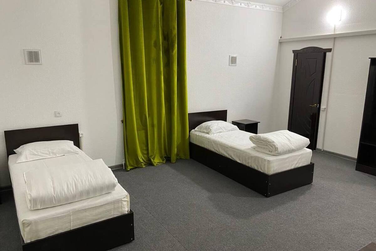 A hotel room with two single beds, a green curtain, a dark door, and a small bedside table.
