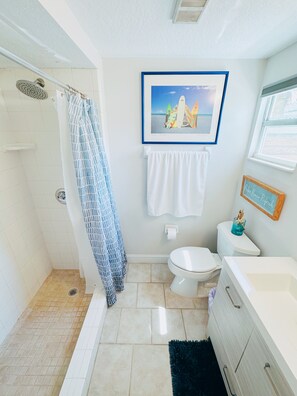A bathroom with a shower, toilet, sink, and a framed picture of surfboards on the wall. - LaLa`s Beach House, Two!  - Walking Distance to the Beach and Great Shopping!  (New Smyrna Beach)