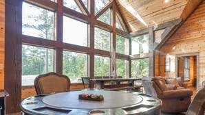 A spacious room with large windows, wooden beams, a round table, and a comfortable seating area. - 5Br cabin with private exterior bar and secret cinema from bunk room! (Broken Bow)
