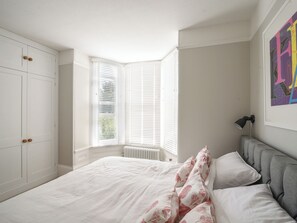 A bedroom with a large bed, white walls, a radiator, and a window with blinds. - Coastal View (Lyme Regis)