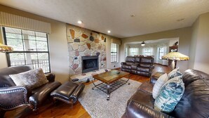 A spacious living room with a stone fireplace, leather sofas, and a large window.