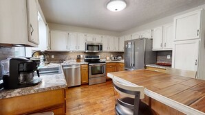 A modern kitchen with white cabinets, stainless steel appliances, and a wooden dining table.