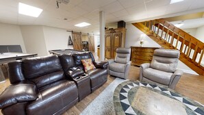 A living room with a pool table, leather sofas, a patterned rug, and a staircase.