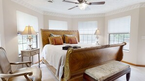 A bedroom with a large bed, two bedside tables with lamps, a chair, a bench, and a ceiling fan.