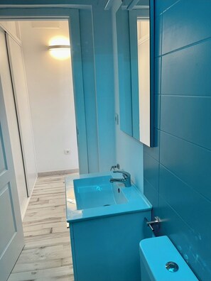Une salle de bain avec un lavabo bleu, un miroir et un luminaire fixé au mur.