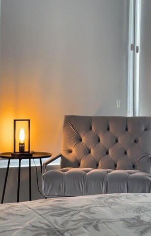 Une chambre à coucher avec une tête de lit capitonnée, une table de chevet avec une lampe et une vue sur l’extérieur par une fenêtre.