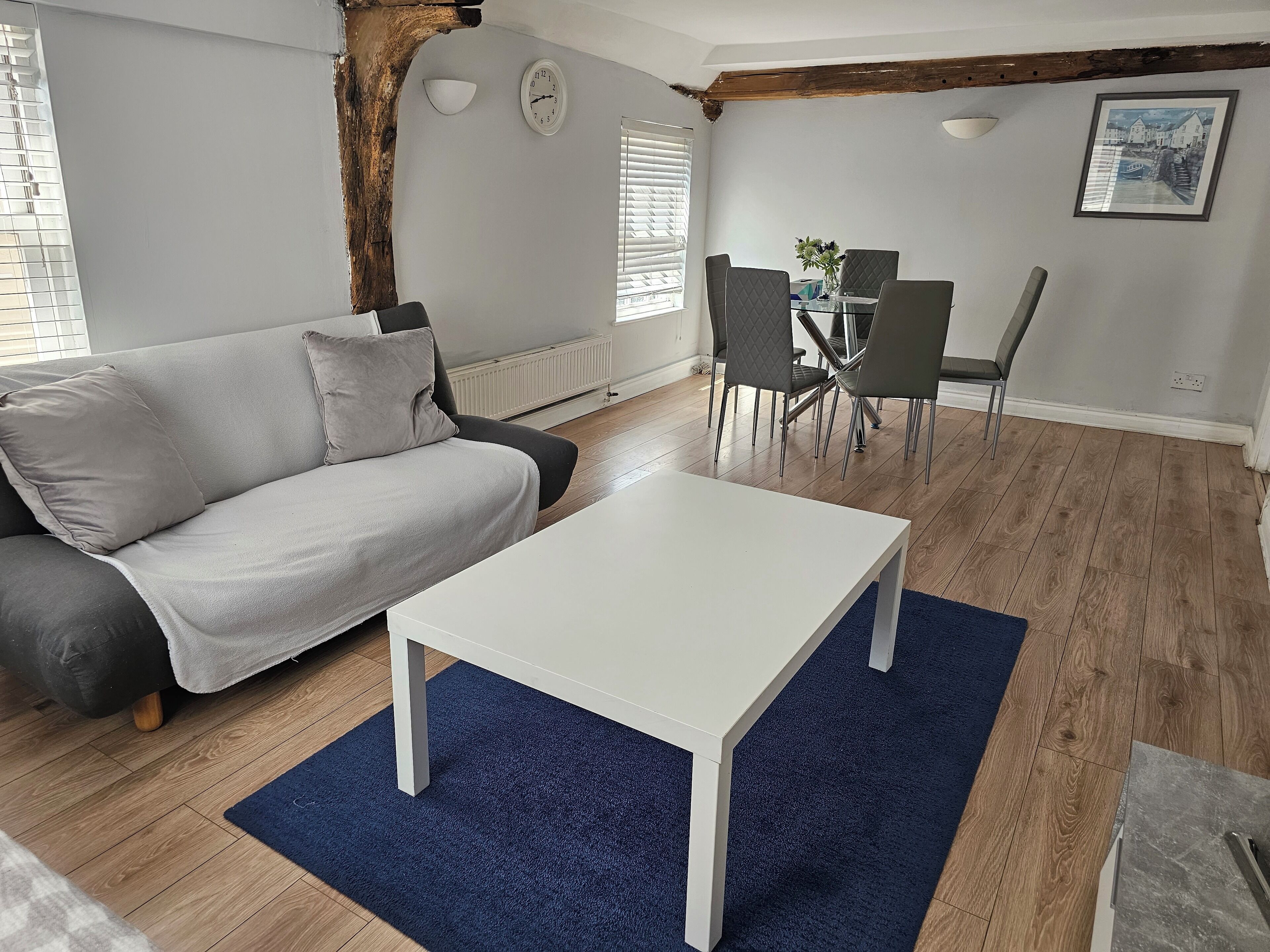 A living room with a grey sofa, a white coffee table, and a dining area with chairs and a table.