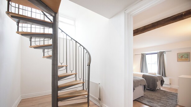 Een trap met houten treden en metalen leuningen, die leidt naar een slaapkamer met een bed en een radiator.