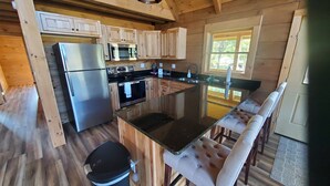 A compact kitchen with wooden cabinets, a stainless steel refrigerator, a microwave, and a sink.