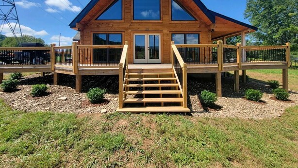 A wooden cabin with a steeply pitched roof, a front porch, and a staircase leading to the entrance.