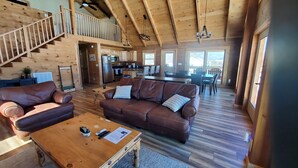 A spacious living area with a wooden staircase, a kitchen, and a dining area.