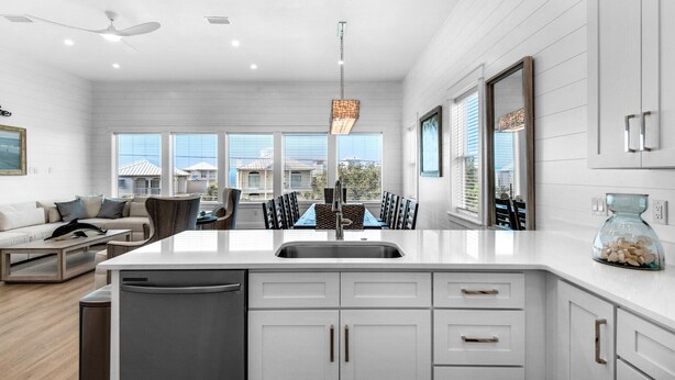 A modern kitchen with white cabinetry, a central island with a sink, and a dining area with chairs and a table. - NEW!! Horizon! Private Beach ! Golf Cart ! Pool (Santa Rosa Beach)