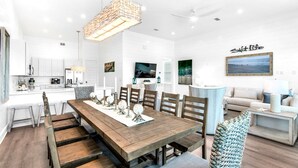 A spacious living area with a large wooden dining table, a comfortable sofa, and a TV mounted on the wall. - NEW!! Horizon! Private Beach ! Golf Cart ! Pool (Santa Rosa Beach)