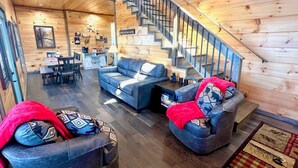 A cozy cabin interior with a staircase, wooden walls, a sofa set, and a dining area. - Bearly Behaving (Sevierville)