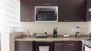 A modern kitchen with dark cabinetry, a built-in microwave, a gas stove, a toaster, and a coffee maker. - Designful Apartment in Trendy Roma Norte/Condesa (Ciudad de México)