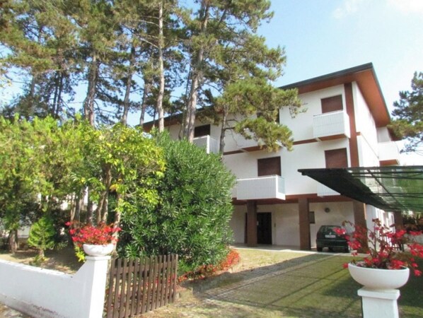 A multi-story building with balconies, surrounded by trees and a fenced garden area. - Welcoming Apartment Near the Beach (San Michele al Tagliamento)