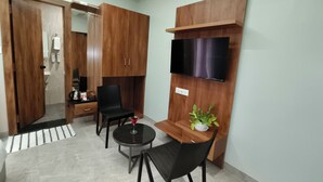 Un espacio habitable pequeño con un armario de madera, una mesita con una silla, un televisor montado en la pared y una planta en maceta.