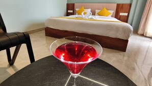Habitación de hotel con cama, una mesita de vidrio y una bebida roja, además de una silla.