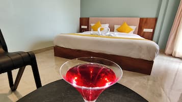 Habitación de hotel con cama, una mesita de vidrio y una bebida roja, además de una silla.