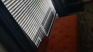 A room with a window with horizontal blinds, a black metal rack, and a red upholstered sofa.