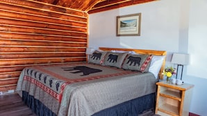 A wooden cabin-style bedroom with a bed, pillows, a nightstand, and a framed picture on the wall. - Big Medicine Cabins (St. Ignatius)