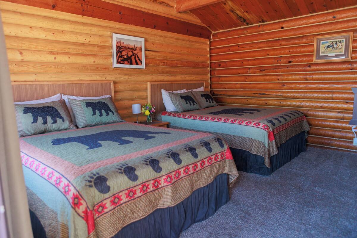 Quarto de cabana rústica com duas camas, cada uma com colcha temática de ursos.