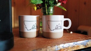 Two mugs with a mountain outline design on a wooden surface. - Big Medicine Cabins (St. Ignatius)