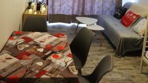 Un espacio habitable compacto con una mesa de comedor, dos sillas, un sofá con cojines, una mesita auxiliar con objetos decorativos y una lámpara en el techo.