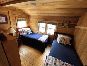 Cozy cabin with two single beds, a dresser, and a chair, perfect for a small group of travelers.