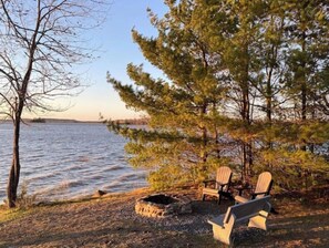 Relax in serene surroundings with Adirondack chairs near a fire pit overlooking the tranquil lake.